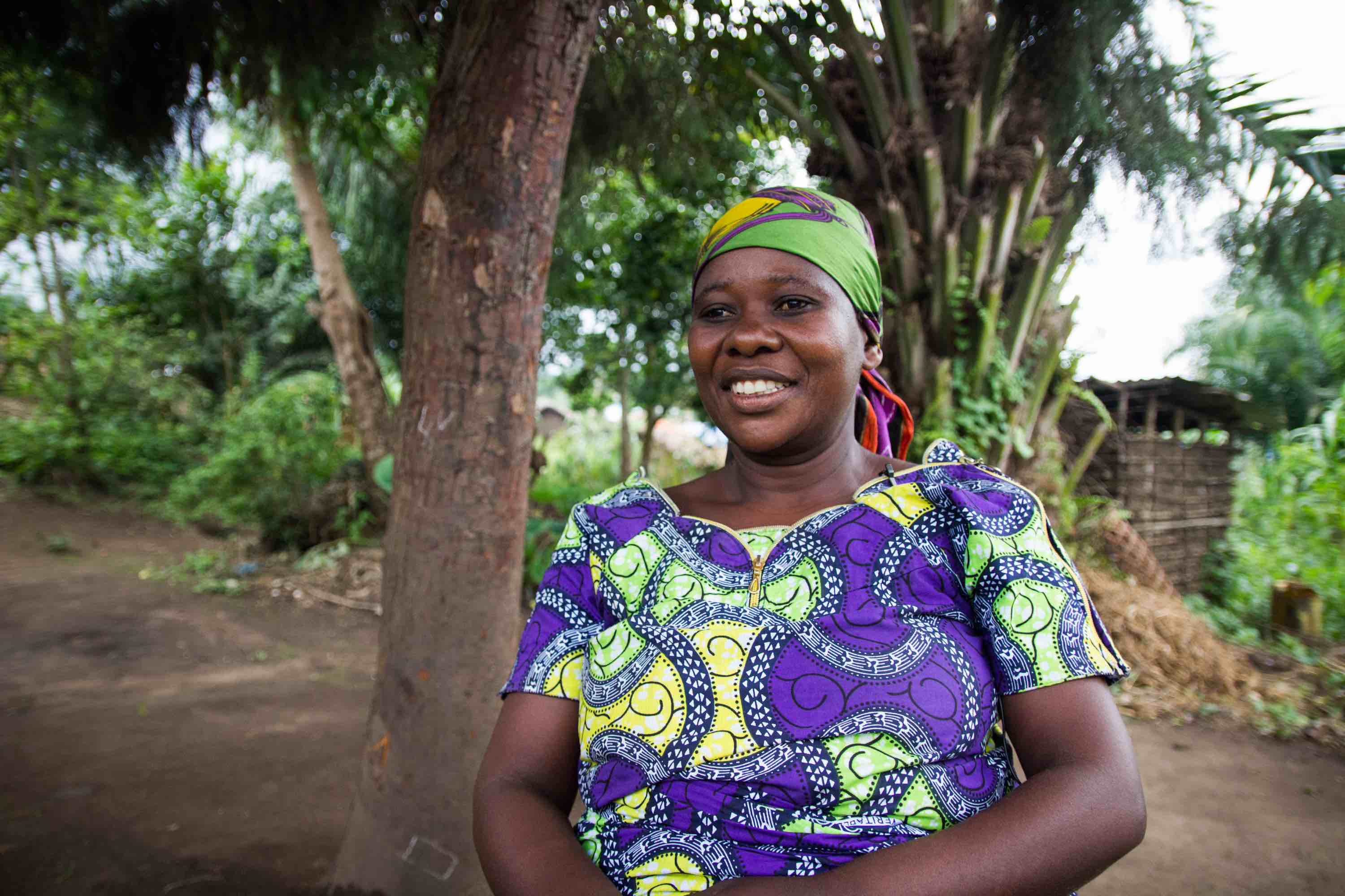 Sarah stands in front of her home in Azoo, DRC.